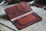 A WM Leatherwork Collection - Premium Leather Field Notes Wallet from Rogue Industries lies open on a wooden surface, showcasing several card slots and a pocket. Various leatherworking tools are scattered in the background.