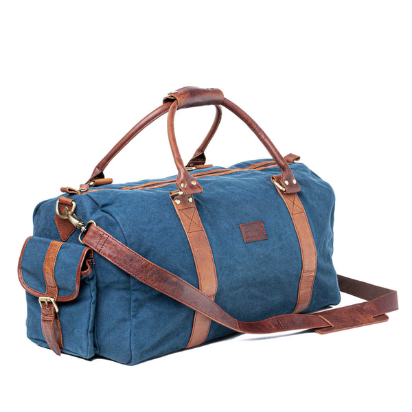 A White Cap Waxed Canvas Duffle by Rogue Industries with brown full grain leather handles and straps, featuring a side pocket with a buckle closure and a detachable shoulder strap. This water-resistant bag is both stylish and durable for any adventure.