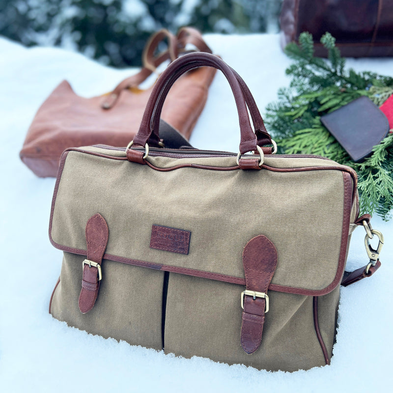 The Rogue Industries Waxed Canvas Laptop Bag rests on snow next to some greenery and another brown bag.