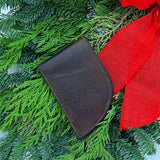 The Rogue Industries Front Pocket Wallet - Classic Made in Maine Edition rests elegantly on a green pine wreath with a red ribbon. Crafted from brown leather, this RFID-blocking cardholder combines style and security seamlessly.